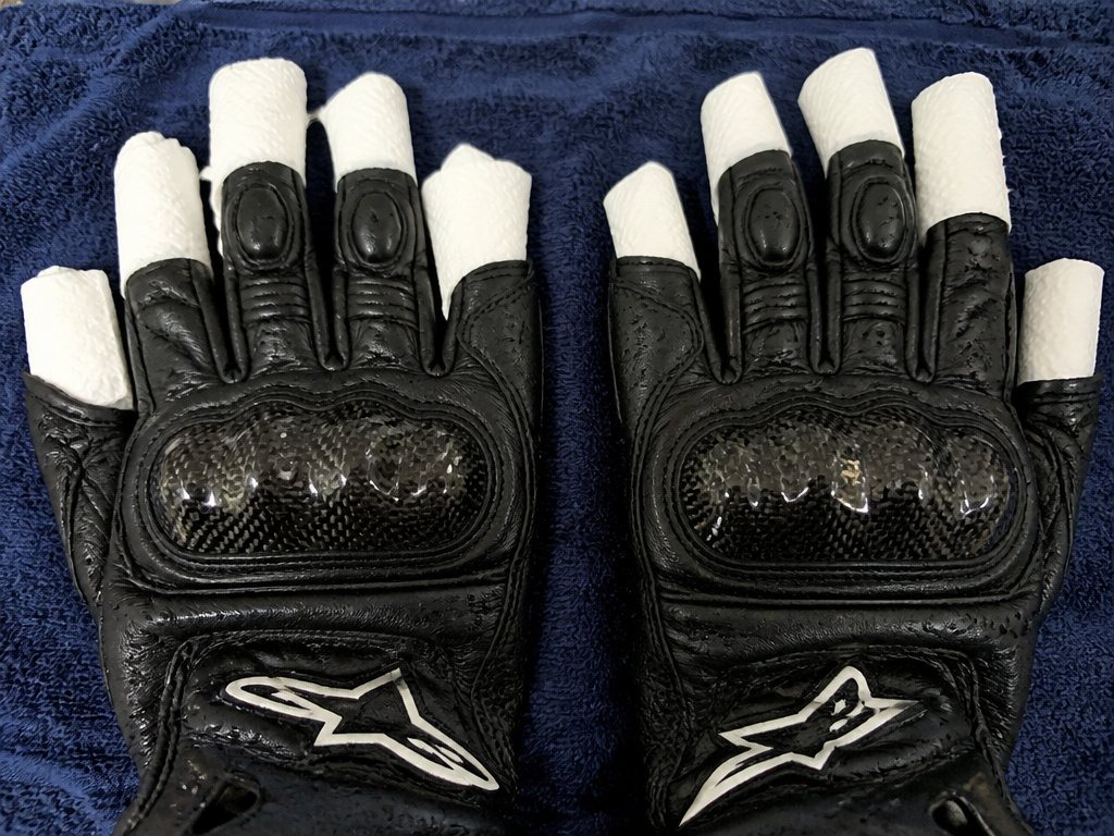 Properly shaped leather motorcycle gloves drying flat on a dark towel.